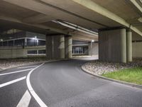 the empty road is under a very overpass that has an overhead lamp beside it