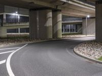 the empty road is under a very overpass that has an overhead lamp beside it