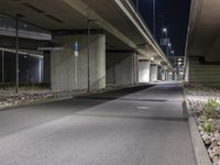 the empty road is under a very overpass that has an overhead lamp beside it