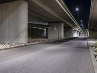 the empty road is under a very overpass that has an overhead lamp beside it