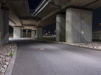 the empty road is under a very overpass that has an overhead lamp beside it