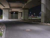 the empty road is under a very overpass that has an overhead lamp beside it