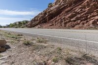 an empty road next to a red rock mountain and blue sky with clouds and a yellow border