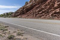 an empty road next to a red rock mountain and blue sky with clouds and a yellow border