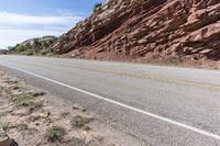 an empty road next to a red rock mountain and blue sky with clouds and a yellow border