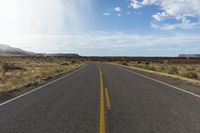 an empty road stretches along the side of a hill near a grassy field with desert and rocks