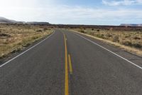 an empty road stretches along the side of a hill near a grassy field with desert and rocks