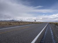 a view of an empty road with cloudy skies above it and mountains beyond the stretch