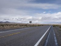 a view of an empty road with cloudy skies above it and mountains beyond the stretch