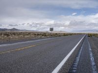 a view of an empty road with cloudy skies above it and mountains beyond the stretch