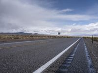 a view of an empty road with cloudy skies above it and mountains beyond the stretch