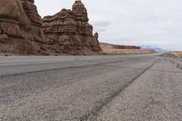 an empty road in the middle of the desert with rocks on both sides and mountains behind it