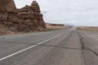 an empty road in the middle of the desert with rocks on both sides and mountains behind it