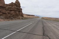 an empty road in the middle of the desert with rocks on both sides and mountains behind it