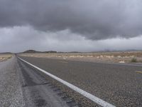 a empty road with some trees in the distance under a cloudy sky in the desert