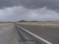 a empty road with some trees in the distance under a cloudy sky in the desert