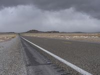 a empty road with some trees in the distance under a cloudy sky in the desert