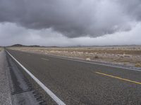 a empty road with some trees in the distance under a cloudy sky in the desert