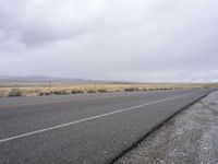 an empty road and two lanes in the desert on a grey day with the sky and clouds overhead