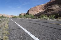 empty road leading down to mountains with white stripes on both sides of roadway with shrubs and shrubs