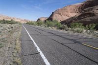 empty road leading down to mountains with white stripes on both sides of roadway with shrubs and shrubs