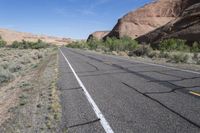 empty road leading down to mountains with white stripes on both sides of roadway with shrubs and shrubs