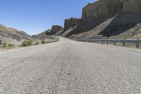 an empty road with signs in the desert with cliffs and blue sky behind it,