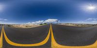 an empty road and blue sky with a few clouds in the background and a few yellow lines on each