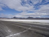 the empty road goes down into the vast plain in front of a mountain range and snow capped mountains