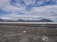 the empty road goes down into the vast plain in front of a mountain range and snow capped mountains