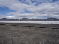 the empty road goes down into the vast plain in front of a mountain range and snow capped mountains