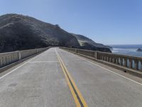 the road is empty and there is no cars on it near the water and mountains