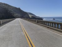 the road is empty and there is no cars on it near the water and mountains