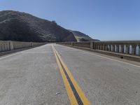 the road is empty and there is no cars on it near the water and mountains