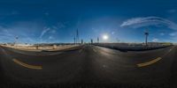 fisheye lens of empty road with yellow lines under blue sky and sun above it