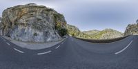 two empty roads next to rocks in a mountainous area with trees and grass on both sides