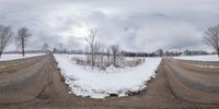 a couple of empty roads surrounded by snow filled ground and trees in the background with no leaves