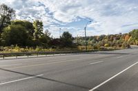 an empty roadway with white markings and yellow lines along it, with trees and blue sky above