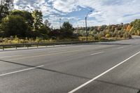 an empty roadway with white markings and yellow lines along it, with trees and blue sky above