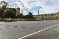 an empty roadway with white markings and yellow lines along it, with trees and blue sky above