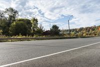 an empty roadway with white markings and yellow lines along it, with trees and blue sky above