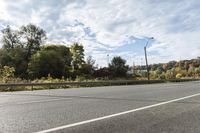 an empty roadway with white markings and yellow lines along it, with trees and blue sky above