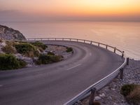 an empty roadway on a cliff overlooking the ocean at sunset with a bird flying over the edge