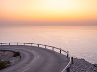 an empty roadway on a cliff overlooking the ocean at sunset with a bird flying over the edge