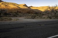 an empty roadway is in the middle of a desert landscape with mountains, trees and grass