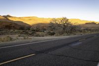 an empty roadway is in the middle of a desert landscape with mountains, trees and grass