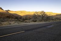 an empty roadway is in the middle of a desert landscape with mountains, trees and grass