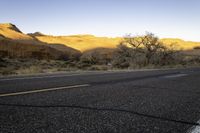 an empty roadway is in the middle of a desert landscape with mountains, trees and grass