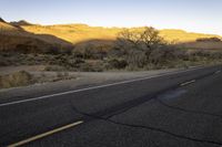 an empty roadway is in the middle of a desert landscape with mountains, trees and grass