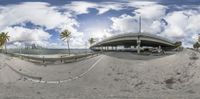 a fish eye view of an empty roadway by the ocean with palm trees in the background